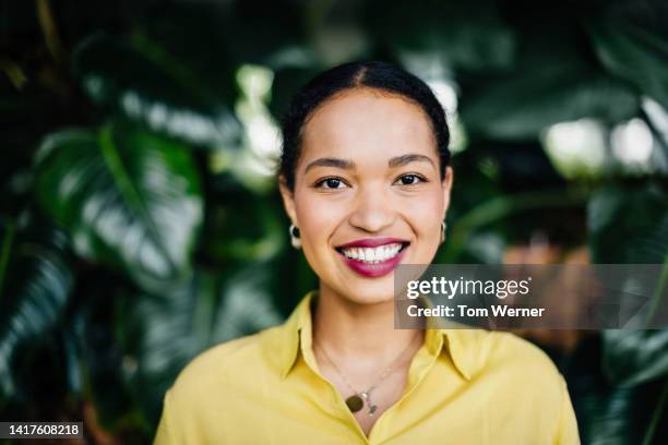 portrait of office manager  smiling in front of large, leafy plants - bright colours happy stock-fotos und bilder