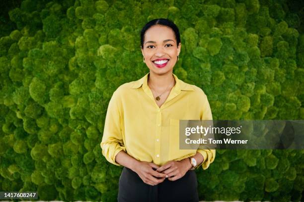 portrait of woman standing in front of mossy backdrop - gelbe bluse stock-fotos und bilder