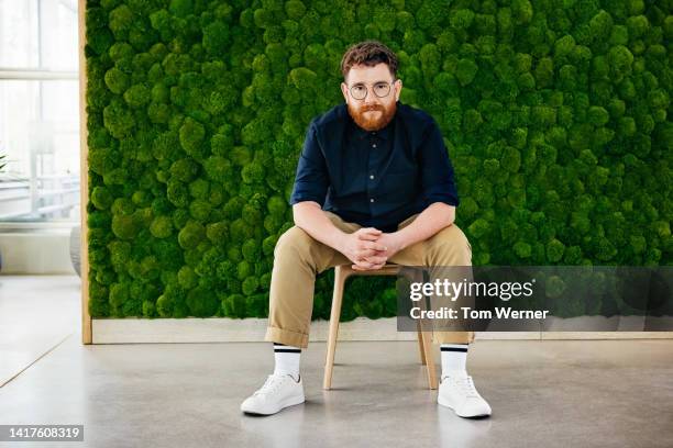 portrait of office manager with beard sitting in front of large mossy backdrop - gelassene person stock-fotos und bilder