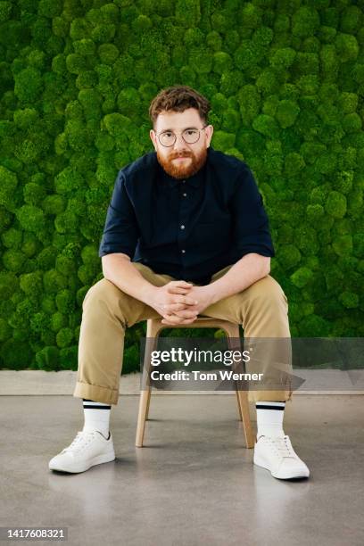 portrait of office employee sitting in front of large mossy backdrop - beige pants stock-fotos und bilder