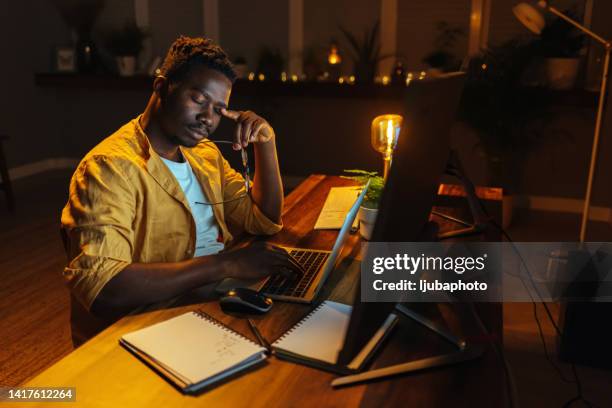 homme africain qui s’ennuie de travailler sur un ordinateur portable à la maison - fond usé photos et images de collection