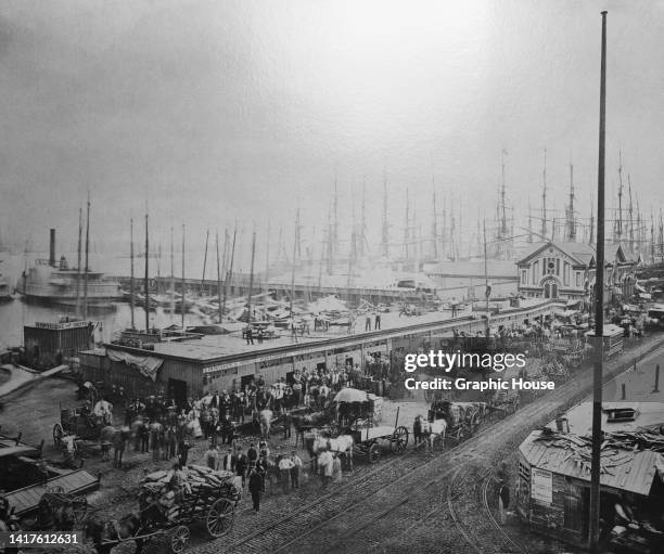 View of dock workers and ships beyond, with the Fulton Ferry Terminal, Pier Seventeen, and the Fulton Fish Market on the East River, in South Street,...