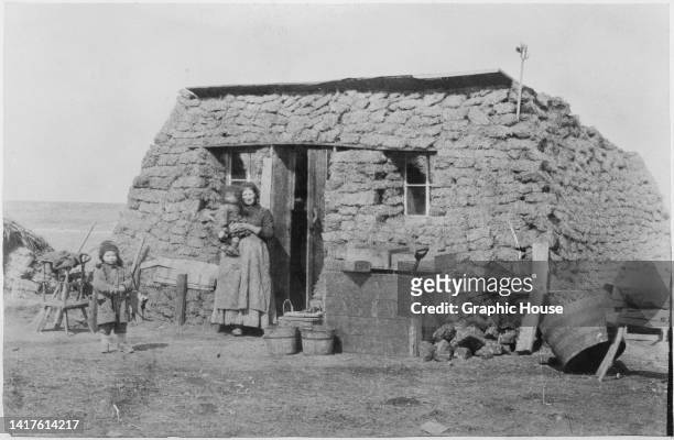 Woman and children standing by the doorway of a sod house, constructed from sods of earth, prairie grass being in abundance for settlers, Dakota...
