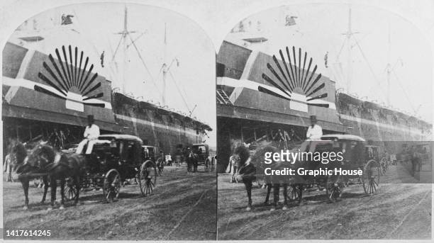 Stereoscopic image showing the a horse and carriage passing one of the paddle wheels of the SS Great Eastern, an iron steamship designed by Isambard...