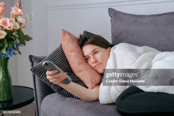 cold at home young woman on the couch, covered with a warm blanket and switching tv channels, it's cold at home - zapper photos et images de collection