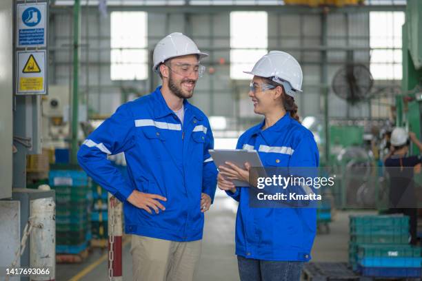 two production engineers talking while standing in front of stamping machine in a factory. female engineer holding digital tablet. - igualdad de género fotografías e imágenes de stock