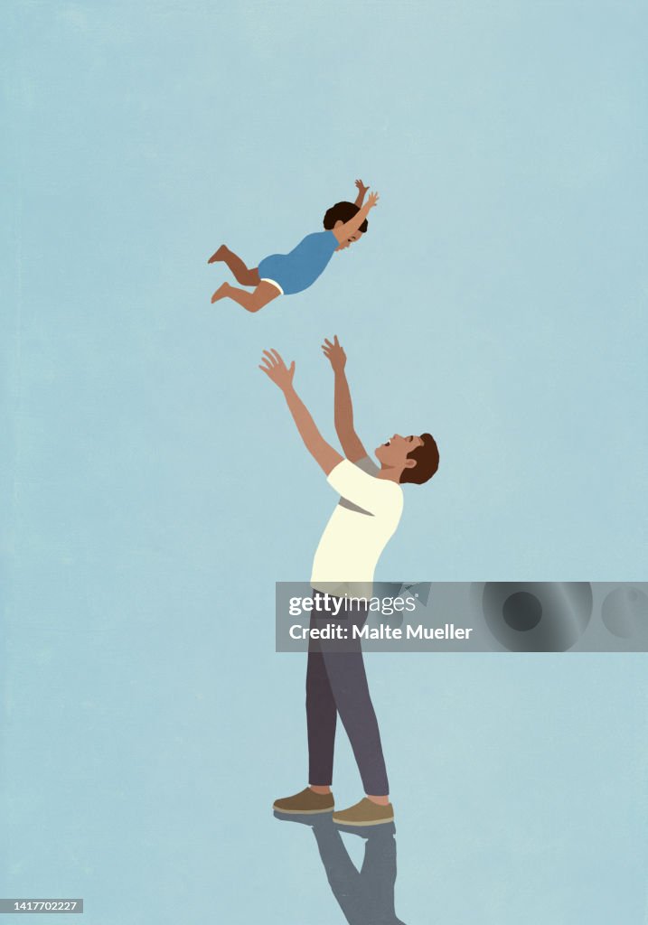 Playful father throwing toddler son overhead on blue background