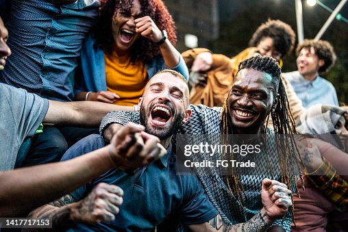 Des amis qui regardent un match de sport et célèbrent le plein air Des amis qui regardent un match de sport et célèbrent le plein air