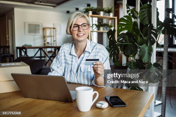 young blonde woman holding her credit card and smiling - loyalty program stock pictures, royalty-free photos & images