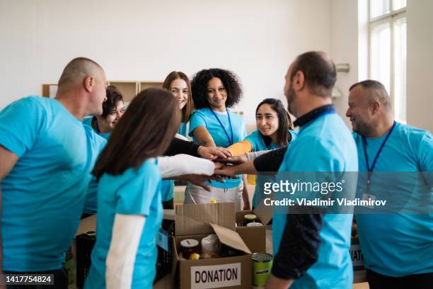 a circle of aid workers celebrating by stacking their hands together - philanthropist stock pictures, royalty-free photos & images