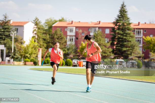 teen boys passing the relay baton on the track field - stafett bildbanksfoton och bilder