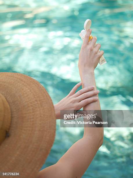 woman in hat rubbing sunscreen onto skin. - headwear stock-fotos und bilder