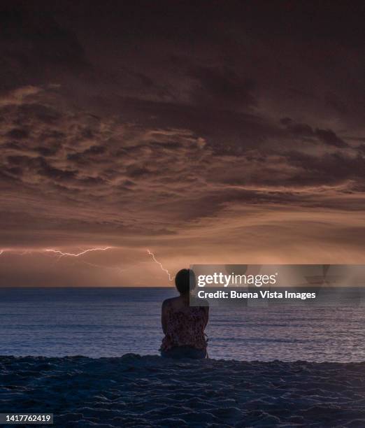 woman on a beach watching thunderstorm over the sea - watching thunderstorm stock pictures, royalty-free photos & images