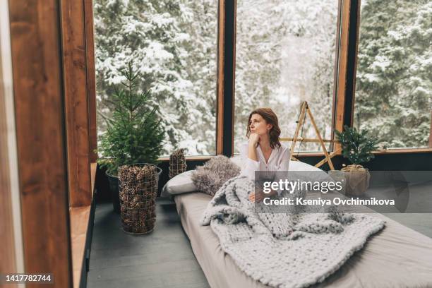 cozy woman in knitted winter warm socks and sweater with sleeping dog and checkered plaid holding a cup of hot cocoa or coffee, during resting on couch at home in christmas holidays. winter drinks. - wool blanket stock pictures, royalty-free photos & images