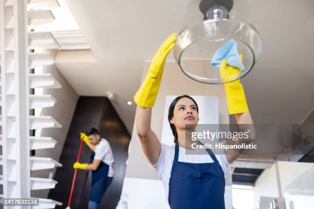 housekeeper cleaning a glass lamp at a house - janitorial services stockfoto's en -beelden