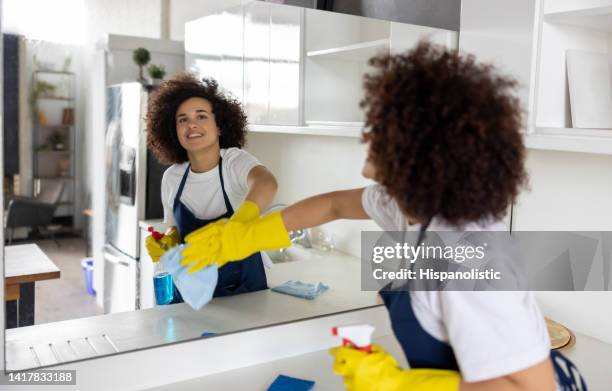 glückliche reinigungskraft beim reinigen eines spiegels in der küche - cleaner man uniform stock-fotos und bilder