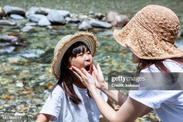 asian mother putting sunscreen on daughter's face at the river - cream colored hat stock pictures, royalty-free photos & images