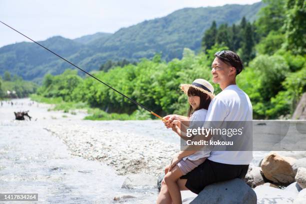 若い父親と幼い娘が川岸で釣りをしています。 - outdoor pursuit ストックフォトと画像