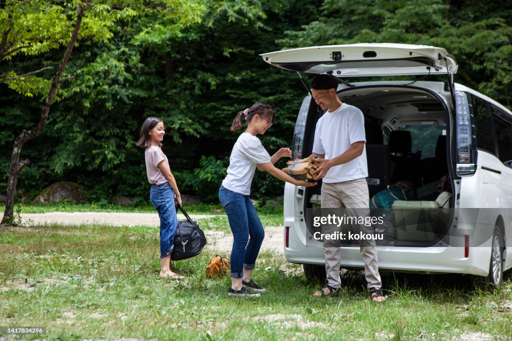 A father and his two daughters prepare to build a tent at a campsite.