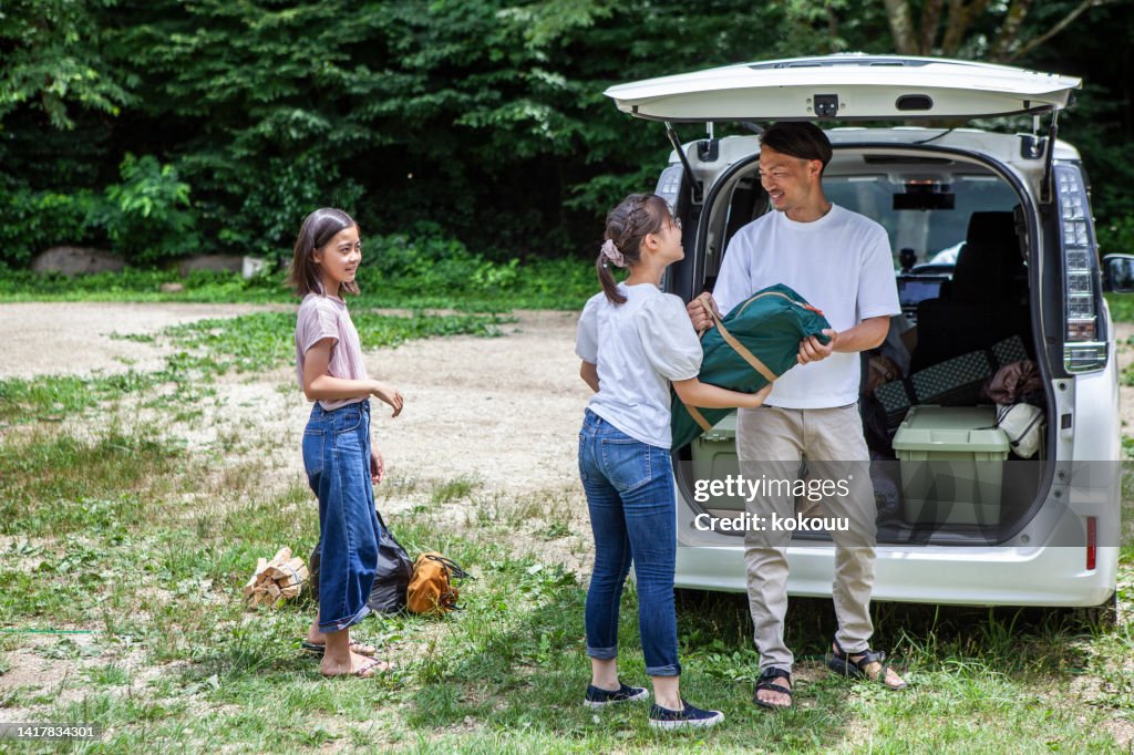 A father and his two daughters prepare to build a tent at a campsite.