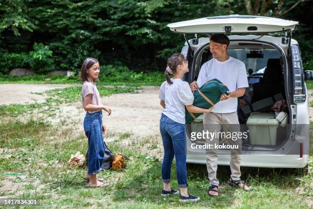 a father and his two daughters prepare to build a tent at a campsite. - japanese tents stock pictures, royalty-free photos & images
