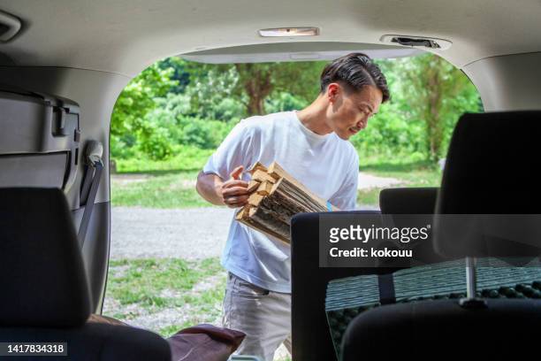 young man carrying camping equipment out of his car. - car camping luggage stock pictures, royalty-free photos & images