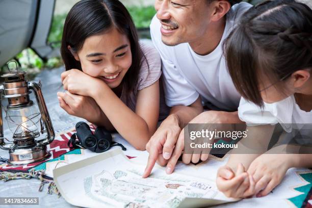 two teenage girls and their father try to riddle in a tent. - camping games stockfoto's en -beelden