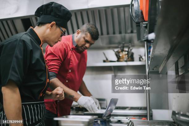 asiatisch-chinesischer männlicher trainee-küchencrew, der vom meisterkoch lernt, der speisen in der großküche zubereitet - kochlehrling stock-fotos und bilder