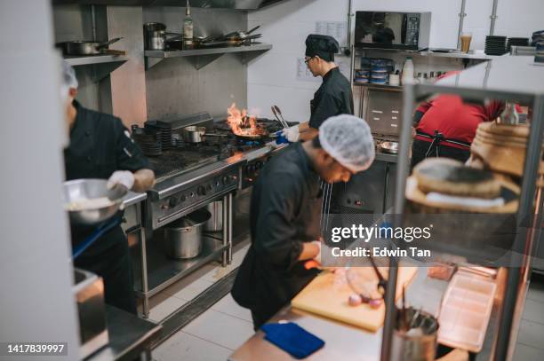 asian chinese chef performing flambe with other crew busy preparing food in kitchen - crew stock pictures, royalty-free photos & images
