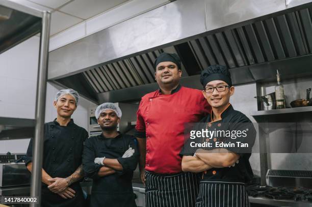 chef indiano asiático e equipe ajudante de cozinha olhando para a câmera sorrindo na cozinha comercial - chef leader - fotografias e filmes do acervo