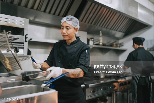 asian kitchen crew dripping dry fried french fries from appliance - hair net stock pictures, royalty-free photos & images