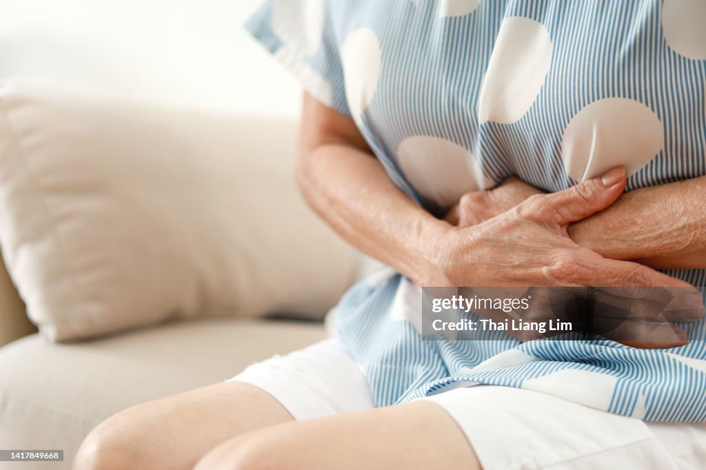 Senior woman having painful stomachache, sitting on sofa at home