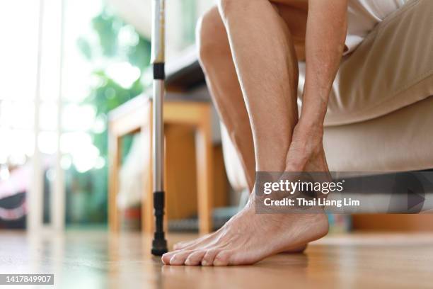 senior woman sitting on sofa holds her ankle injury, feeling pain. - vrist bildbanksfoton och bilder