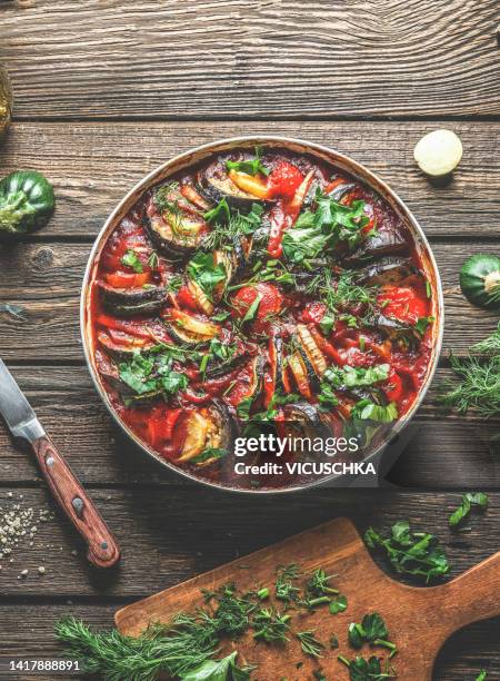 tasty ratatouille in cooking pan on wooden table with seasoning and kitchen utensils. - ratatuia foto e immagini stock