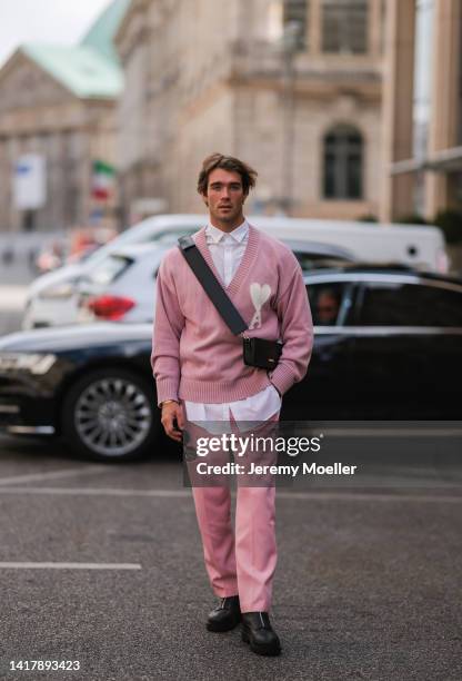 Janis Danner is seen wearing Ami Paris pink v neckline knit sweater, Jacquemus black bag, Versace black and gold shades, Ami Paris pink matching rose...