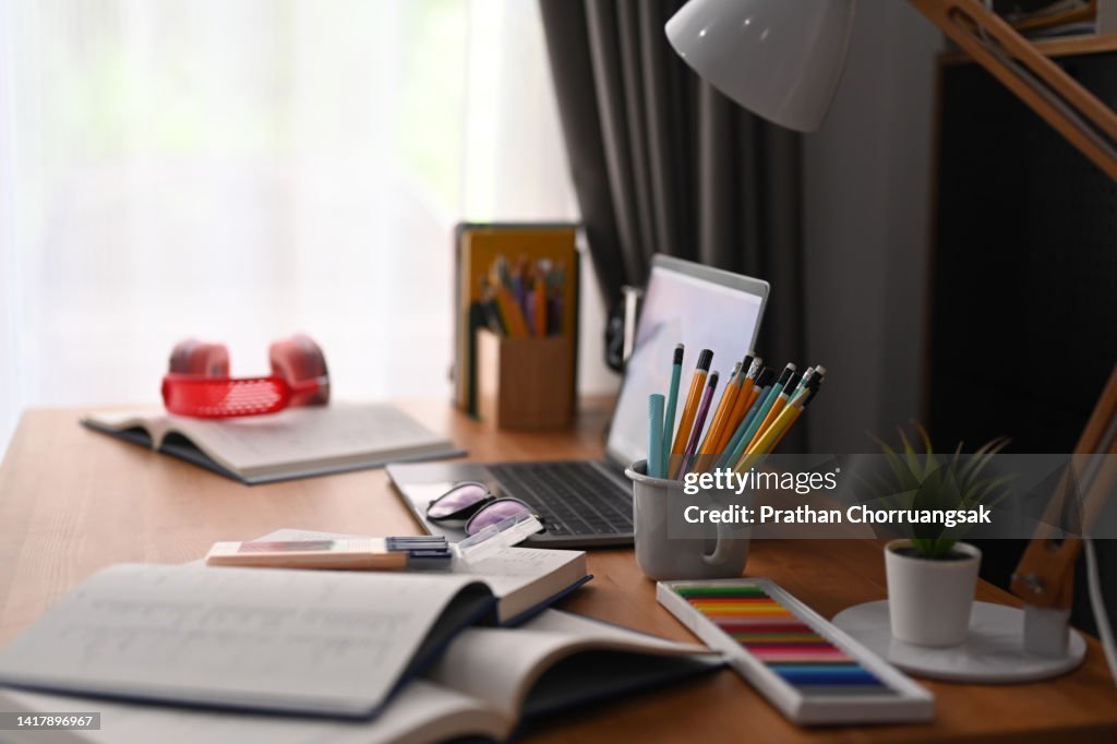 Laptop, various school stationery, headphone and lamp on wooden table.