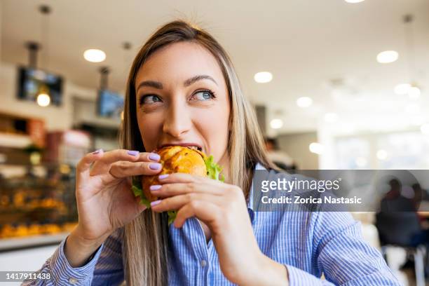 young women eating sandwich looking through window - bakery window stock pictures, royalty-free photos & images