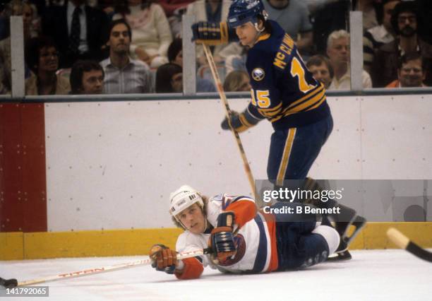 Mike Bossy of the New York Islanders reaches for the puck while on the ground as Rob McClanahan of the Buffalo Sabres skates by him circa 1981 at the...