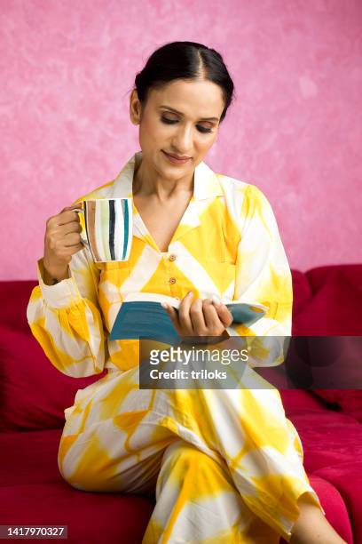 schöne frau, die kaffee trinkt, während sie buch liest - tee indien trinken stock-fotos und bilder