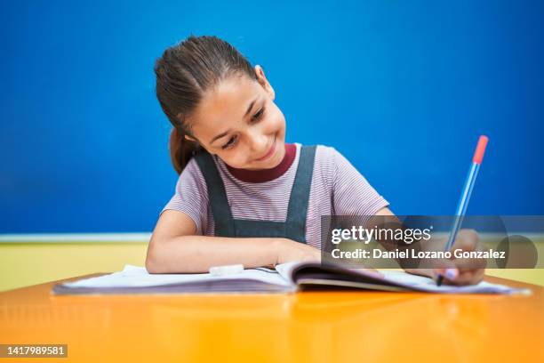 school girl writing in a textbook while sitting in the classroom. - escribir a mano fotografías e imágenes de stock