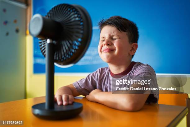 boy refreshing from heat with an electric fan at school. - electric fan stockfoto's en -beelden