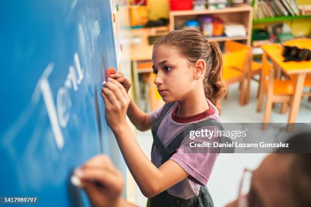 school girl writing on a chalkboard in her classroom. - caligrafia imagens e fotografias de stock