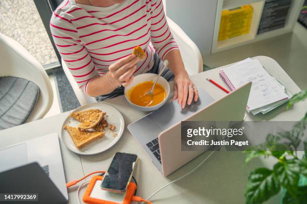 mature woman eating her lunch whilst working from home - gig economy stock pictures, royalty-free photos & images