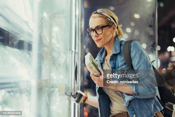 porträt einer schönen frau, die produkte aus einem kühlschrank im supermarkt auswählt - supermarket refrigeration stock-fotos und bilder