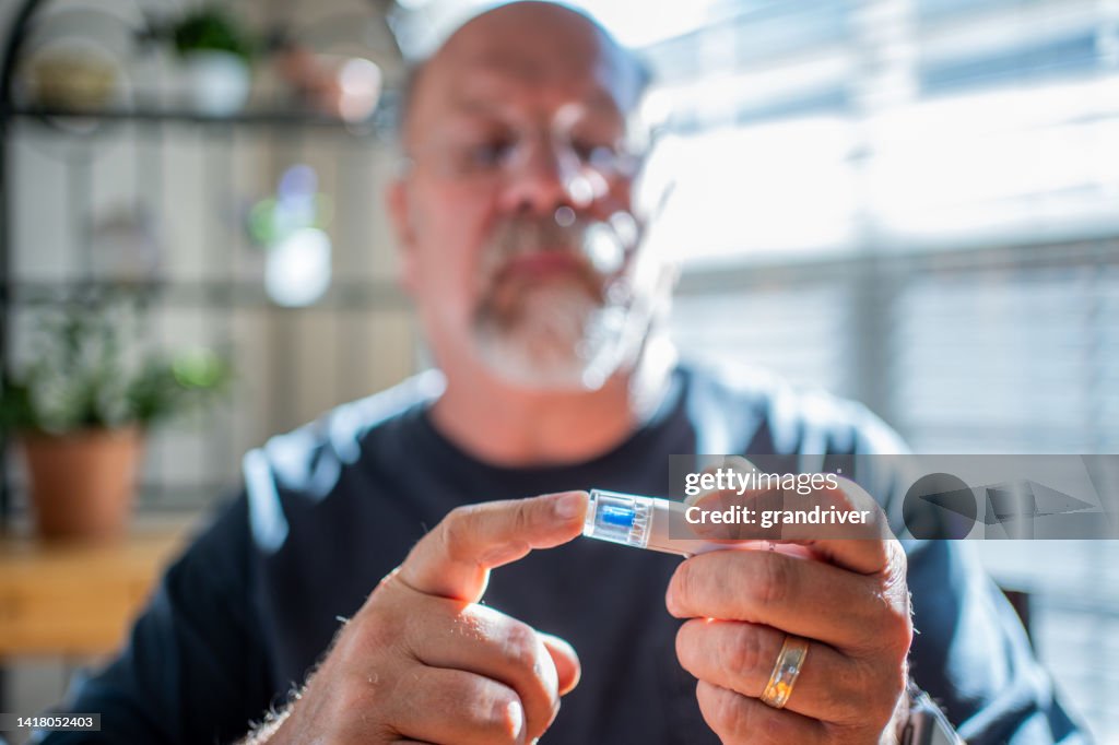 Hombre maduro que revisa su glucosa en sangre con un kit de prueba de glucómetro casero para prevenir el control de la diabetes