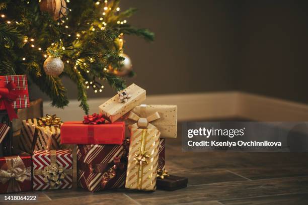 photo of luxury gift boxes under christmas tree, new year home decorations, golden wrapping of santa presents, festive tree decorated with garland, baubles, traditional celebration. copy space - christmas tree presents stock-fotos und bilder