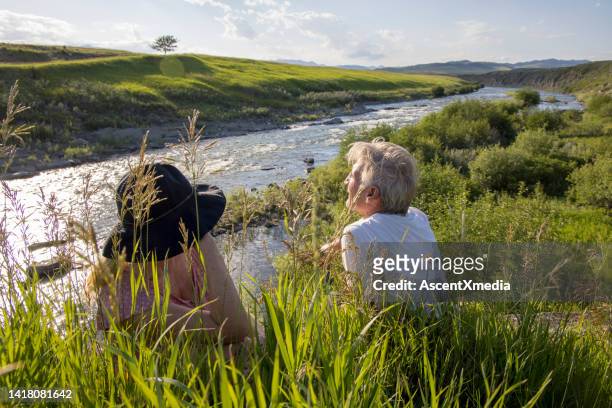 mature couple relax at viewpoint over river - rivier gras oever stockfoto's en -beelden