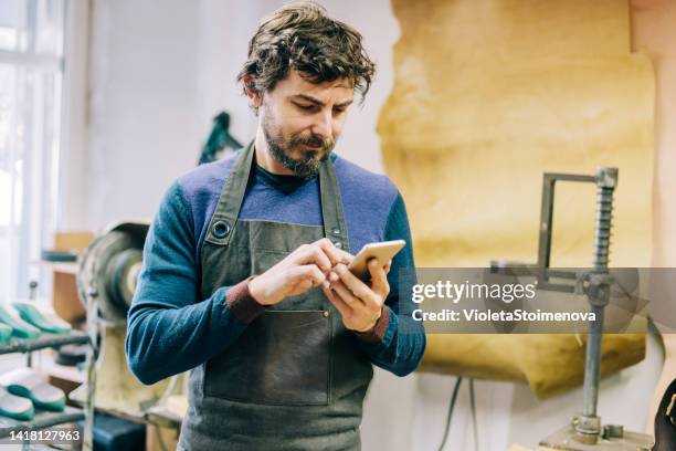 giovane calzolaio che usa lo smartphone nel suo laboratorio. - shoe repair foto e immagini stock