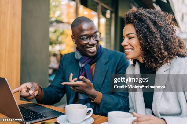 young couple sitting in a sidewalk cafe and using laptop. - coffee shop couple stock pictures, royalty-free photos & images