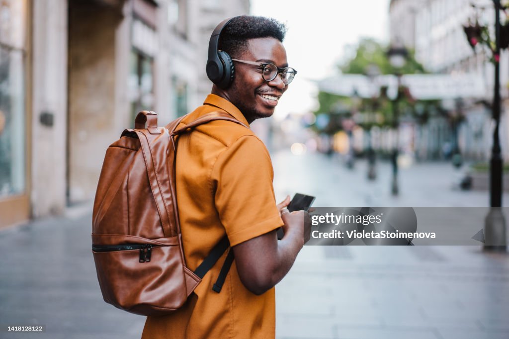 Cheerful young man listening to music while walking on the street.